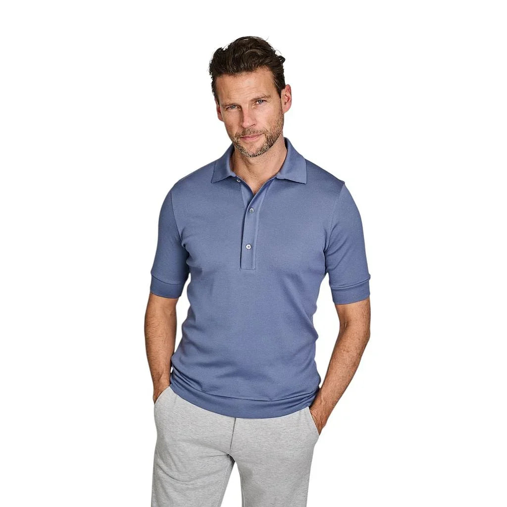 Man in een blauwe polo en een grijze joggingbroek tegen een witte achtergrond.